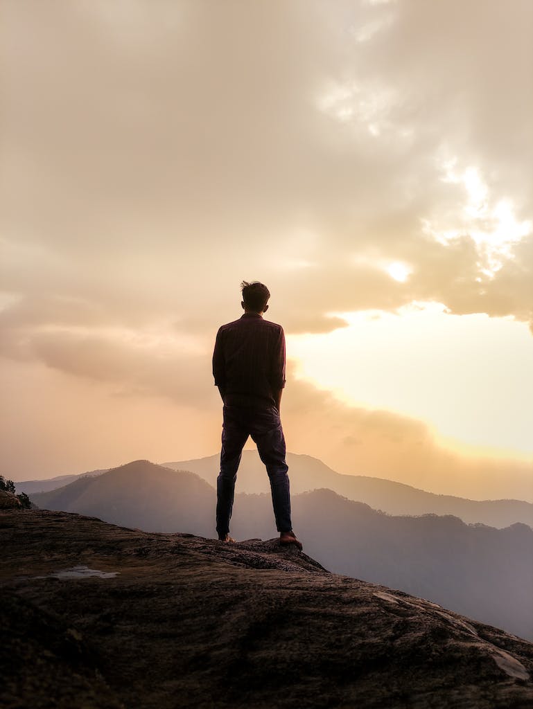 A backlit photo of a man on top of a mountain. 